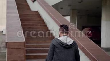 一个穿着灰色连帽衫，穿着<strong>深色</strong>头发的时髦成年<strong>男子</strong>在一家餐馆上楼梯。