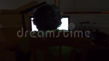男孩使用笔记本电脑在一个黑暗的房间，4k，从后面看