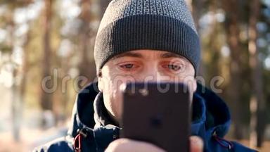 一个穿着温暖衣服的男人，在寒冷的<strong>季</strong>节，用智能<strong>手机</strong>，看着<strong>手机</strong>屏幕。 特写镜头。