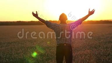 一个年轻的农民站在麦田里，看着夕阳，挥动着他的手。 快乐的商人。