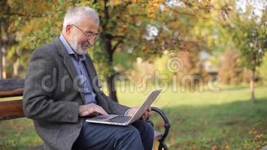 高级商人在外面<strong>用笔</strong>记本电脑。 穿灰色夹克的老人在公园里<strong>用笔</strong>记本电脑