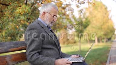 高级商人在外面用笔记本电脑。 穿灰色夹克的老人在公园里用笔记本电脑