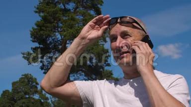 戴眼镜的秃头男子在夏季公园背景下通过手机通话