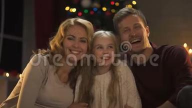 年轻的家庭拥抱，欢笑，看着镜头，圣诞灯光闪闪发光