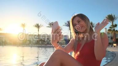 年轻女孩在豪华别墅的游泳池附近放松，通过智能手机与朋友在线视频通话