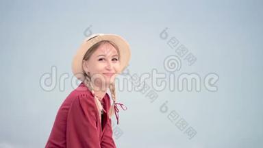 一位美丽的白种人年轻女子，身穿红色连衣裙，头戴草帽，头戴辫子，坐在，坐在海滨微笑