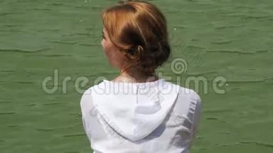 穿着白衬衫的女孩在<strong>江水</strong>背景上享受夏日。 年轻女子在绿湖岸边放松，看着