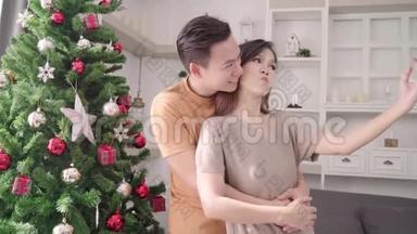 亚洲夫妇使用智能<strong>手机</strong>自拍与圣诞树装饰他们的客厅在家里圣诞<strong>节</strong>。