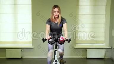 在健身房骑自行<strong>车来</strong>适应年轻女人。 强壮的女运动员在健康俱乐部做循环有氧运动。