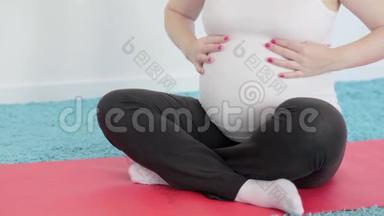 一个怀孕的女孩正在做瑜伽冥想。 肚子里的婴儿推着。 一个女人抚摸她的腹部