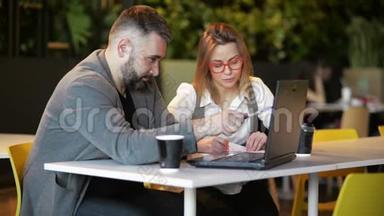 两位年轻的专业人士坐在办公桌前，看着笔记本电脑屏幕，一起讨论项目。 男女工人