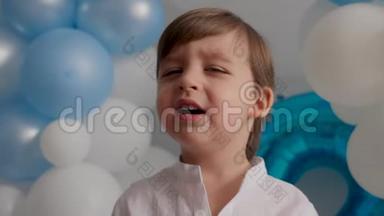 两岁的男孩穿着白色衬衫，穿着蓝色气球坐在家里