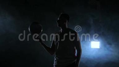 篮球运动员表演不同的技巧和旋转球在黑暗的健身房与烟雾。 慢动作