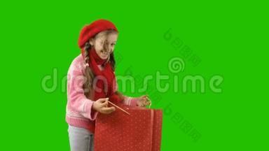 一个十岁左右的女孩戴着一顶红色针织帽子和一<strong>条带</strong>辫子的围巾，手里拿着一个包裹，向她挥手