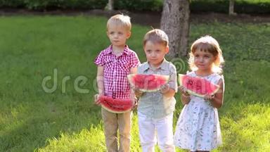 三个可爱的<strong>小孩</strong>子在炎热的天气里在一个<strong>夏天</strong>阳光明媚的公园里吃西瓜。