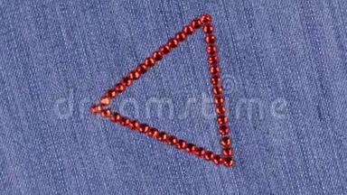 在牛仔布上旋转一个由红色莱茵石制成的三角形，三角形象征着完成。