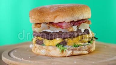 牛肉汉堡，奶酪，酱汁和蔬菜旋转在木板前面的绿色屏幕背景。