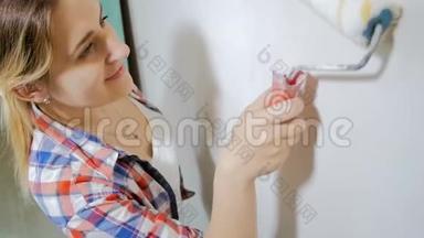 美丽微笑的年轻女子用白色油漆和滚筒在她的房子里画墙的视频