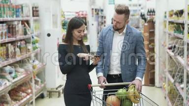 女人用智能手机检查产品清单，男人选择水果，在超市闻一闻。