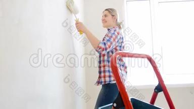 美丽微笑的年轻女子用白色油漆和滚筒在她的房子里画墙的视频