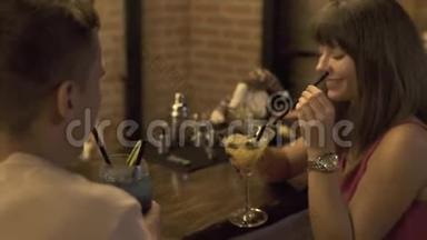 情侣恋爱中的男人和女人喝着酒精鸡尾酒，坐在酒吧柜台，在餐馆浪漫约会。 青年