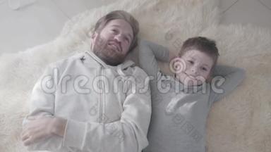快乐的微笑爸爸和他快乐的儿子躺在毛皮地毯上。 <strong>父子</strong>关系。 <strong>父子</strong>关系。