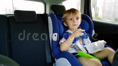 小蹒跚学步的男孩在车里吃饭的4k视频。 儿童坐在安全的汽车座椅上，吃饼干