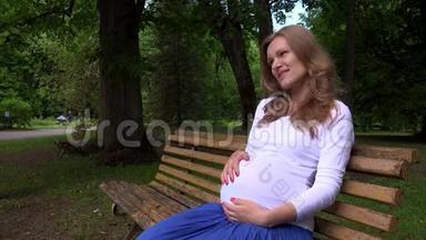 快乐的孕妇坐在长凳上，梦想着在公园<strong>抚摸</strong>她的肚子