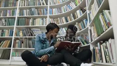 多莉拍摄的非洲年轻男女学生坐在<strong>书架</strong>旁的地板上<strong>看书</strong>。