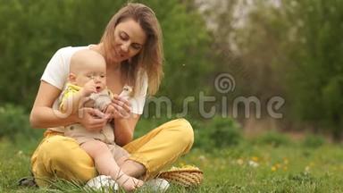 年轻的妈妈带着小宝宝在公园里。 孩子手里拿着蒲公英。 黄绿色配色方案.. 母亲节