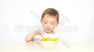 一个快乐和快乐的孩子在白色背景下坐在桌子旁吃<strong>薯片</strong>。