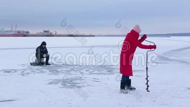 穿着红色保暖夹克和毛毡靴的漂亮渔夫们在冰冻的河流中用冰钻为冰上捕鱼打了个洞
