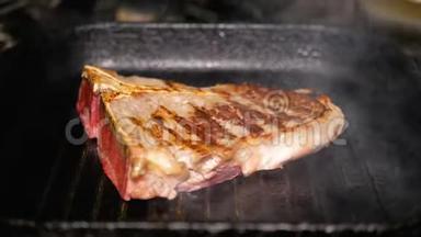 一块生肉用金属钳在烤盘上转动。 烹饪T面牛排特写.. 美味的脂肪垃圾食品。
