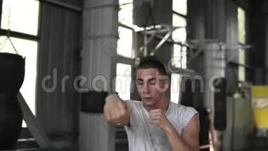一个穿白色T恤的男拳击手的肖像与一个看不见的对手踢，躲避，模仿拳击。 取暖