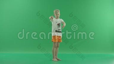 一个身穿便服的金发小男孩正竖起大拇指. 他侧着身子站在绿色屏幕上