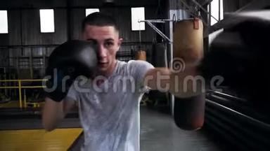 男拳击手手套和白色T恤训练在健身房，拳和上勾拳，运动精神。 正面观点