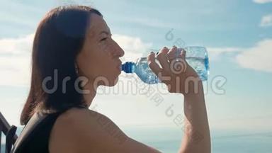 女旅行者带着背包从瓶子里喝水。 健康的徒步旅行女孩在大自然中喝水。