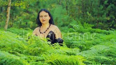 一个穿着黑色衣服的年轻的微笑女巫从一丛蕨类植物中站起来，伸展开来。 万圣节。 哥迪克风格。