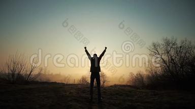 快乐成功的人在日出或日落时庆祝。 快乐自由。 他举起双手，再次欢呼