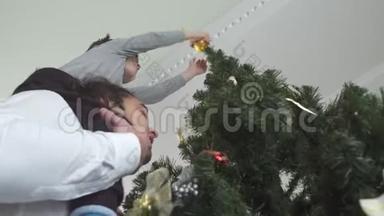 快乐的孩子把圣诞玩具挂在树上，坐在他父亲的脖子上。 父子关系