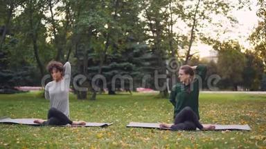 勤奋的瑜伽学生正在学习牛脸的位置，坐在垫子上，伸展手臂，而有经验的老师。