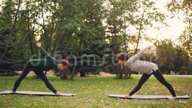 瑜伽学生在户外锻炼，教练伸展双腿，背部向前弯曲，站在绿色的垫子上
