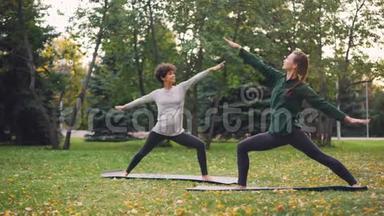 两位美丽的女孩<strong>瑜伽</strong>老师和<strong>学生</strong>正在公园里练习站立在垫子上和移动身体的体式序列