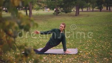 漂亮的年轻女子专注于瑜伽练习，伸展腿，平衡瑜伽垫训练，独自在公园里。
