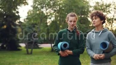 漂亮的女孩在公园里散步，手里拿着瑜伽垫，谈论着<strong>运动器材</strong>，笑着笑着