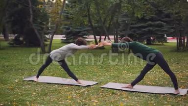 苗条的年轻女士正在公园户外训练，在两人练习时一起做哈他瑜伽，呼吸新鲜空气