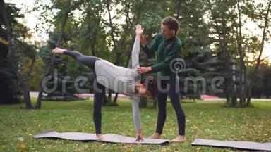 友好的瑜伽教练正在帮助女学生保持半月姿势Ardha Chandrasana站在她身边