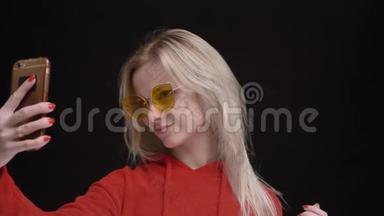 戴着黄色太阳镜的白毛白种人年轻女孩用黑色智能<strong>手机制作</strong>自拍照片的肖像
