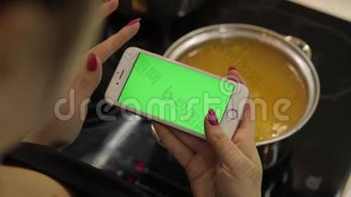 一位女士拿着一部绿色屏幕的智能手机，正在<strong>煮汤</strong>