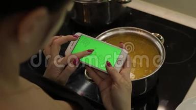 一位女士拿着一部绿色屏幕的智能手机，正在<strong>煮汤</strong>